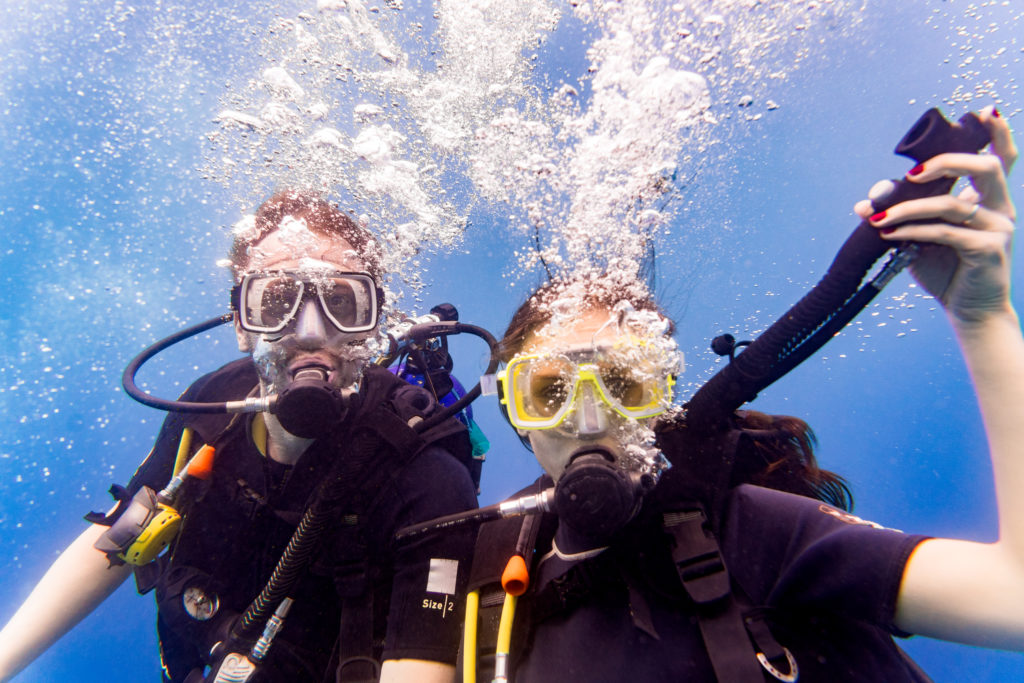 Man and woman scuba divers in tropical sea diving up after underwater excursion
