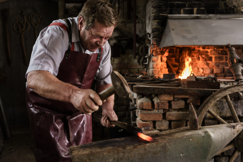 Blacksmith hammering on red hot pick laying on the anvil in his workshop